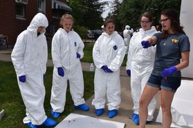 Forensics camp members in crime scene gear, listening to instructor